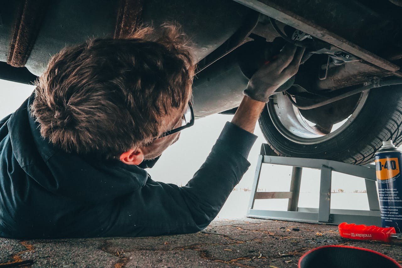 Top 5 Signs Your Car Needs Immediate Attention Mechanic skillfully repairing car undercarriage in outdoor setting with tools.